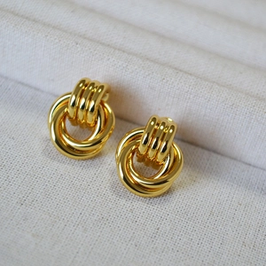 Macro shot of gold-plated multi-layer twisted hoop earrings on linen fabric background