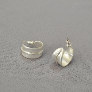 Détail macro de boucles d'oreilles créoles irrégulières en C argent mat brossé