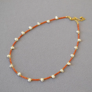 Macro detail of freshwater pearl necklace with orange beads and golden clasp connector