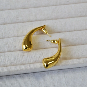 Detailed view of glossy gold-plated horn-shaped teardrop earrings on a beige tray