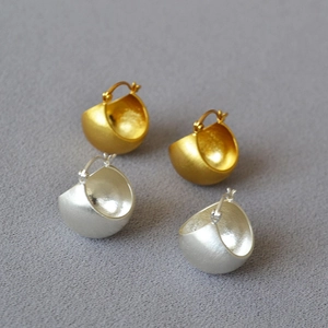 Detailed view of brushed gold and silver hemispherical hoop earrings on grey textured fabric