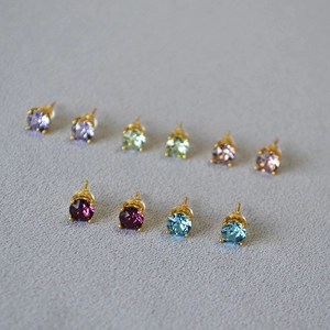 Detailed view of colorful zircon earrings in gold claw settings on gray texture