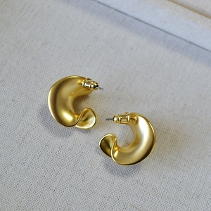 Retro chunky C-shaped matte gold earrings with textured finish on beige fabric background