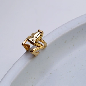 Macro shot of a detailed gold-plated frog ear cuff resting on a ceramic dish edge