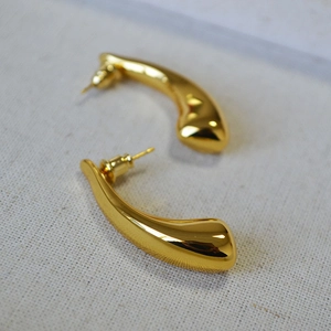 Macro shot of polished gold-plated hollow horn drop earrings on textured fabric