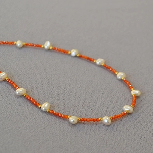 Close-up of beaded necklace featuring baroque pearls, orange faceted beads and gold accents