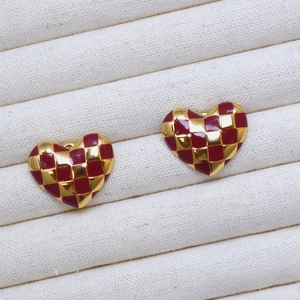 Macro shot of red and gold checkered heart earrings on a white textured jewelry tray