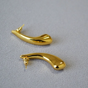 Macro detail of polished gold-plated horn-shaped stud earrings on a gray background