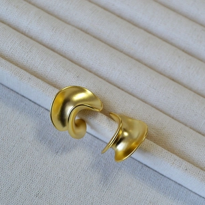 Detailed close-up of matte gold spiral C-shaped earrings with a textured wavy surface