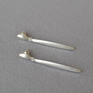 Close-up of minimalist long leaf drop earrings with matte silver finish on grey fabric