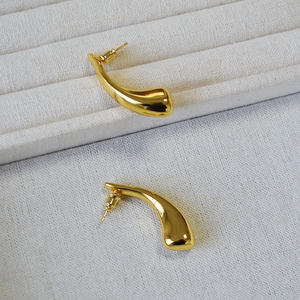 Macro detail of polished gold-plated horn drop earrings on a cream jewelry tray