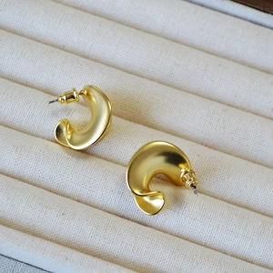Detailed view of twisted golden C-shape earrings with textured matte finish on velvet