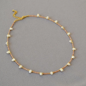 Elegant necklace with pink stone chips, freshwater pearls and gold beads on grey background