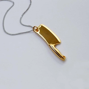 Macro d'un pendentif couperet doré poli miroir avec sa chaîne en argent au style créatif