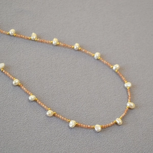 Macro detail of handmade necklace featuring orange sunstone beads and white baroque pearls