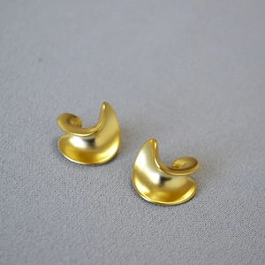 Detail of gold matte earrings with a streamlined twisted C-shape and artistic texture