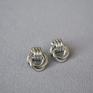 Close-up of polished silver interlaced knot hoop earrings on textured grey fabric