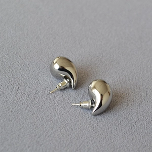 Macro shot of silver-plated hollow teardrop earrings on grey textured fabric background