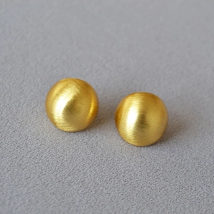 Macro shot of gold ball earrings featuring a brushed metal texture on grey fabric