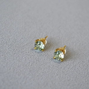 Close-up of light green crystal stud earrings with gold-tone four-prong settings