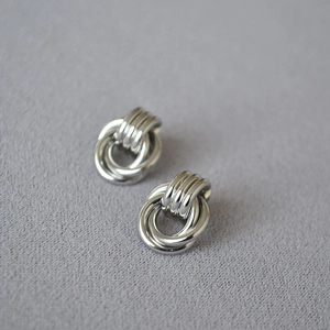 Macro shot of minimalist silver intertwined hoop earrings on grey textured fabric