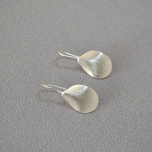 Minimalist silver petal earrings with a brushed metallic texture shown from a top-down view
