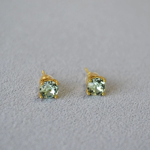 Macro view of light green round crystal earrings with gold four-claw prong setting