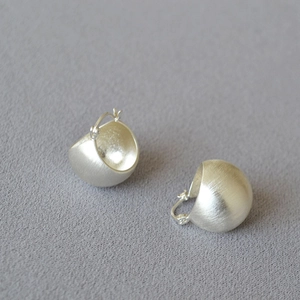 Macro detail of silver spherical earrings featuring a refined brushed metal texture finish