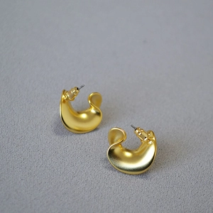 Macro detail of wave-shaped C-style earrings with a matte gold metallic texture
