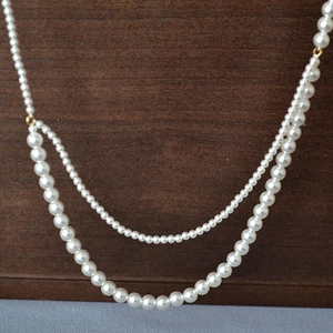 Detail of double-layer faux pearl necklace with gold clasp on wooden and velvet surface