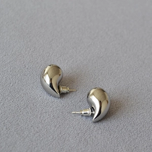 Macro shot of silver-toned hollow teardrop earrings on textured grey fabric background