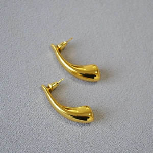 Detail of high-polish gold-plated brass teardrop earrings on grey textured background