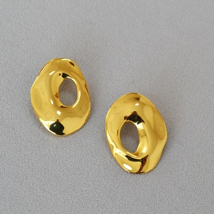 Detailed top view of gold irregular hollow geometric earrings on grey textured fabric