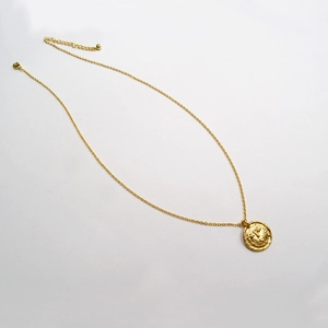 Détail d'un collier en laiton doré vintage avec un pendentif pièce en relief martelé