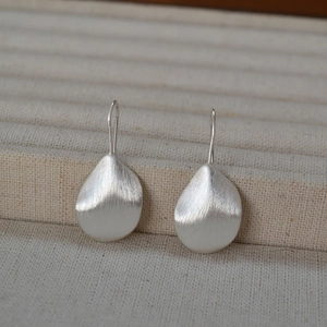 Minimalist silver petal earrings with matte brushed texture on beige linen display stand