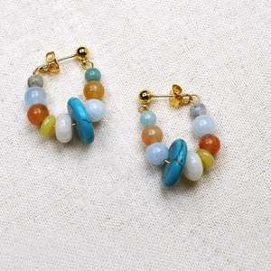 Detail shot of colorful beaded C-shape earrings with gold plated hooks on woven background