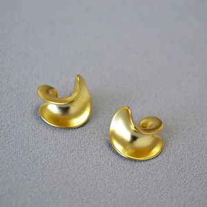 Macro view of gold-plated twisted C-shaped earrings with a matte brushed metal finish
