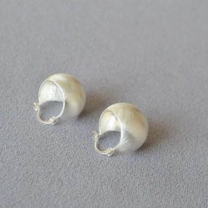 Detailed view of brushed silver ball hoop earrings with a matte metallic texture finish