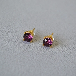Detailed shot of purple crystal stud earrings with gold four-prong setting and silver pins