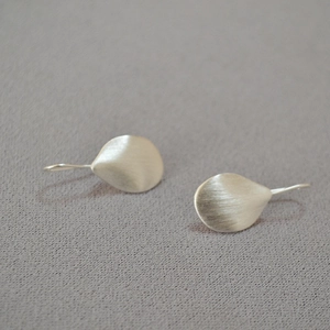 Macro detail of silver petal earrings with brushed matte texture and hook design