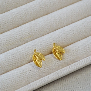 Macro view of gold leaf stud earrings with detailed texture on a soft fabric tray