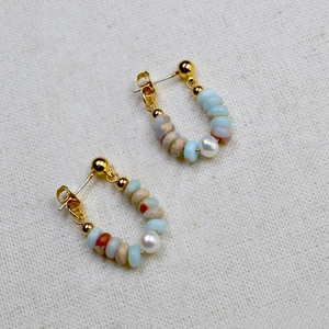 Detail of handmade gold-plated hoop earrings with natural blue and brown beads and white pearl
