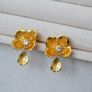 Macro view of gold flower earrings with white zircon center and textured petal drops