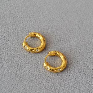 Dettaglio di orecchini placcati in oro con texture martellata e zirconi incastonati