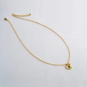 Gros plan d'un pendentif cœur plaqué or avec texture soleil et gemme verte