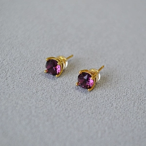 Close-up of purple crystal earrings with gold four-prong setting and silicone backs