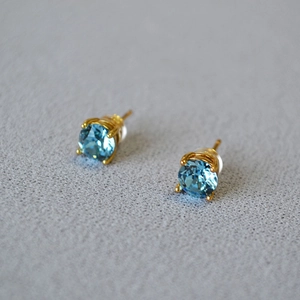 Macro shot of 925 silver stud earrings with blue round-cut crystals and gold claw settings