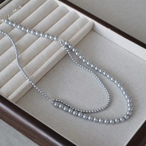 Double-layered gray pearl necklace featuring large and small beads in a wooden jewelry tray