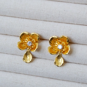 Macro detail of gold-plated flower earrings with matte brushed texture and crystals