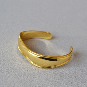 Macro view of wide gold-plated irregular cuff bracelet with polished mirror finish